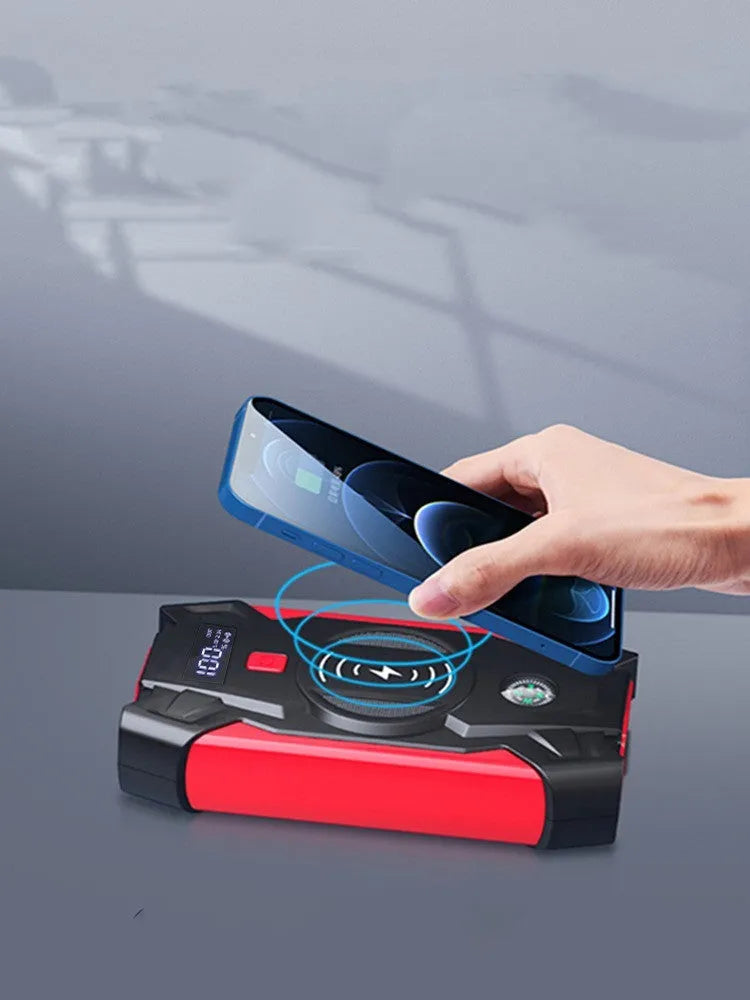 Red car emergency jump starter power pack with battery clamps and cables on a black storage box.