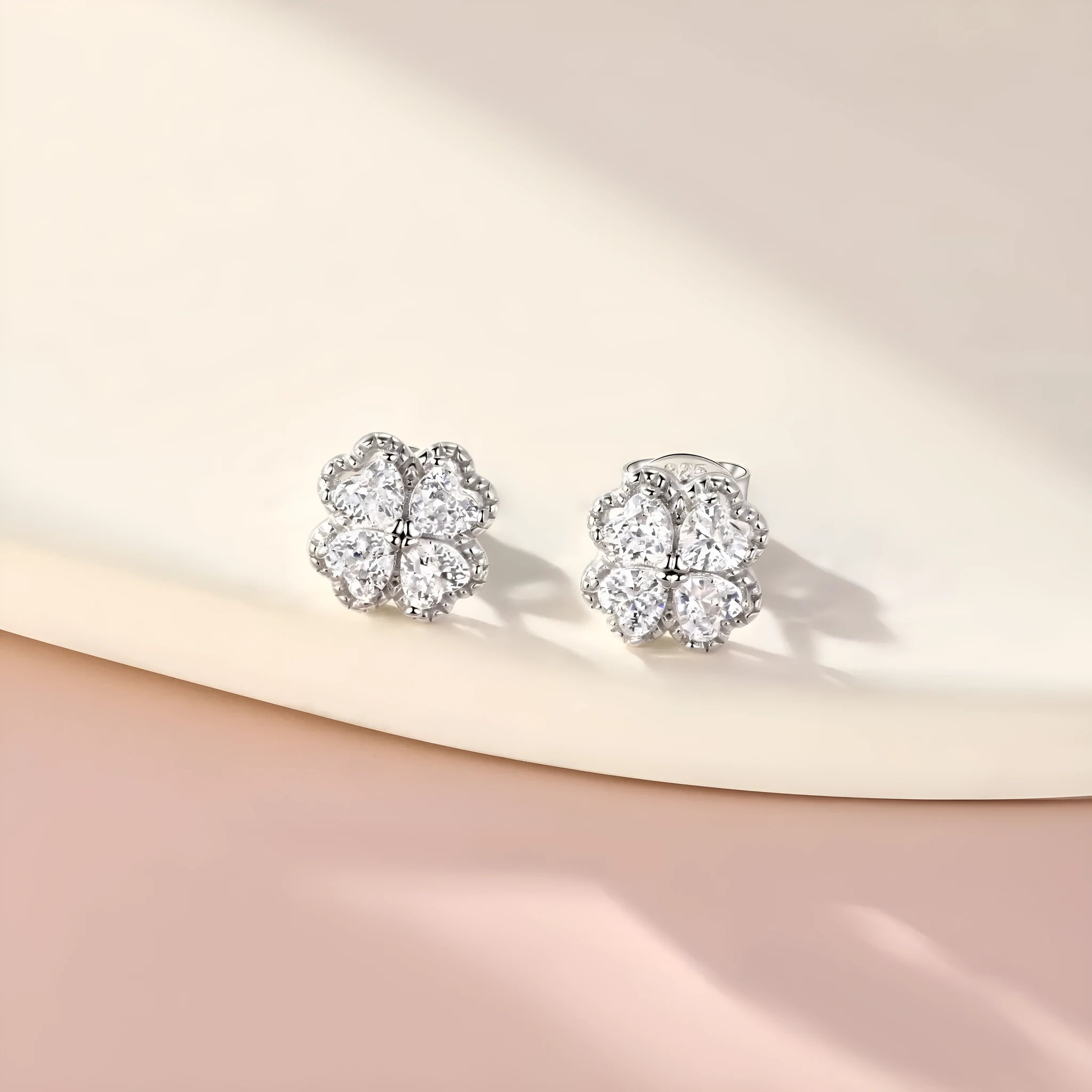 Close-up of a pair of heart-shaped 925 silver earrings with a four-leaf clover charm and zircon stones, in white gold colour.