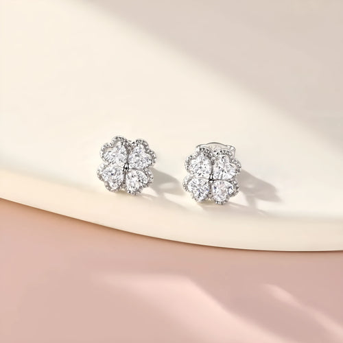 Close-up of a pair of heart-shaped 925 silver earrings with a four-leaf clover charm and zircon stones, in white gold colour.