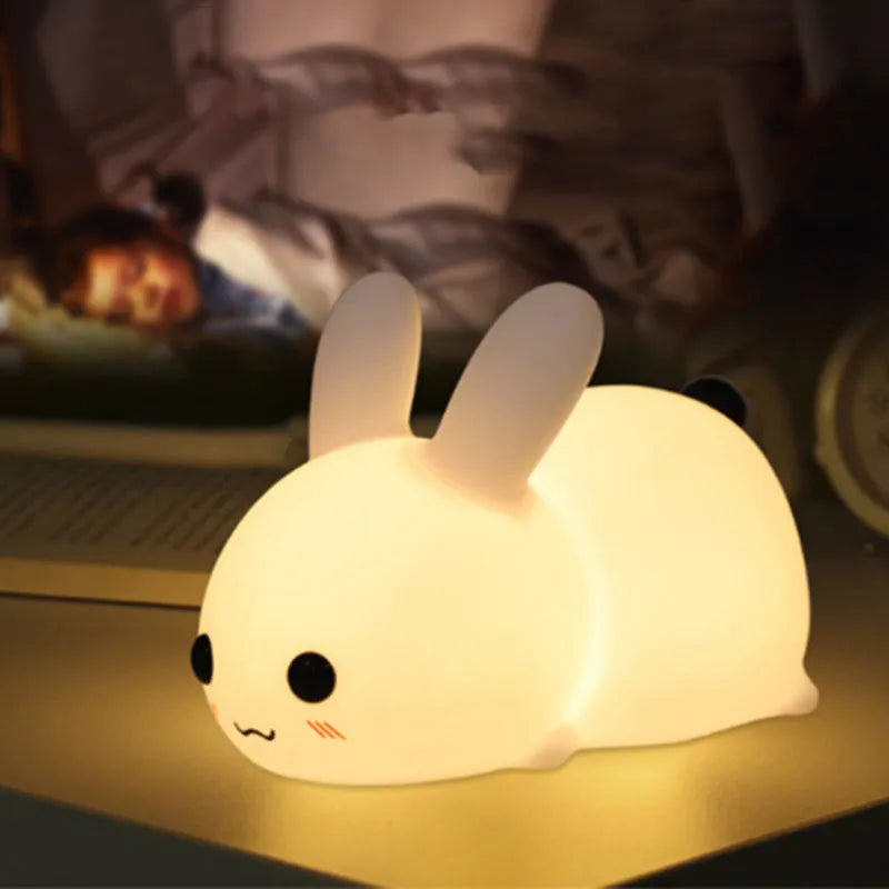 White silicone rabbit night light with warm and white LED glow on a wooden bedside table
