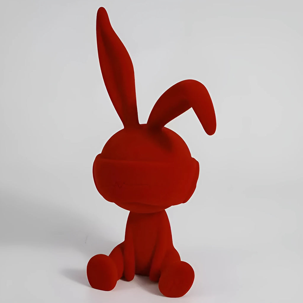Green resin table ornament of a rabbit wearing a suede blindfold on a wooden shelf.