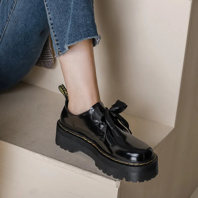 Women's black leather flat shoes with thick soles, cross straps, ribbons, and laced closure.
