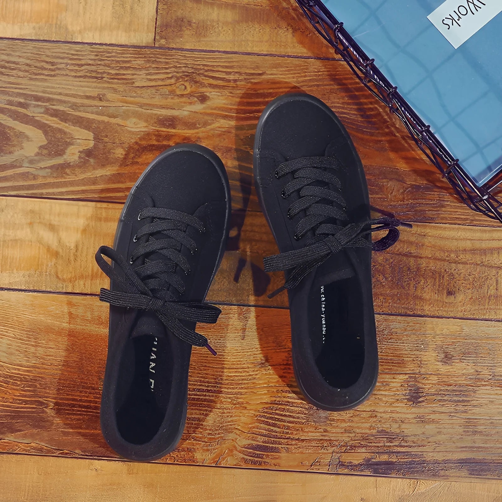 All black low-top canvas flat shoes with white laces and a rubber sole.
