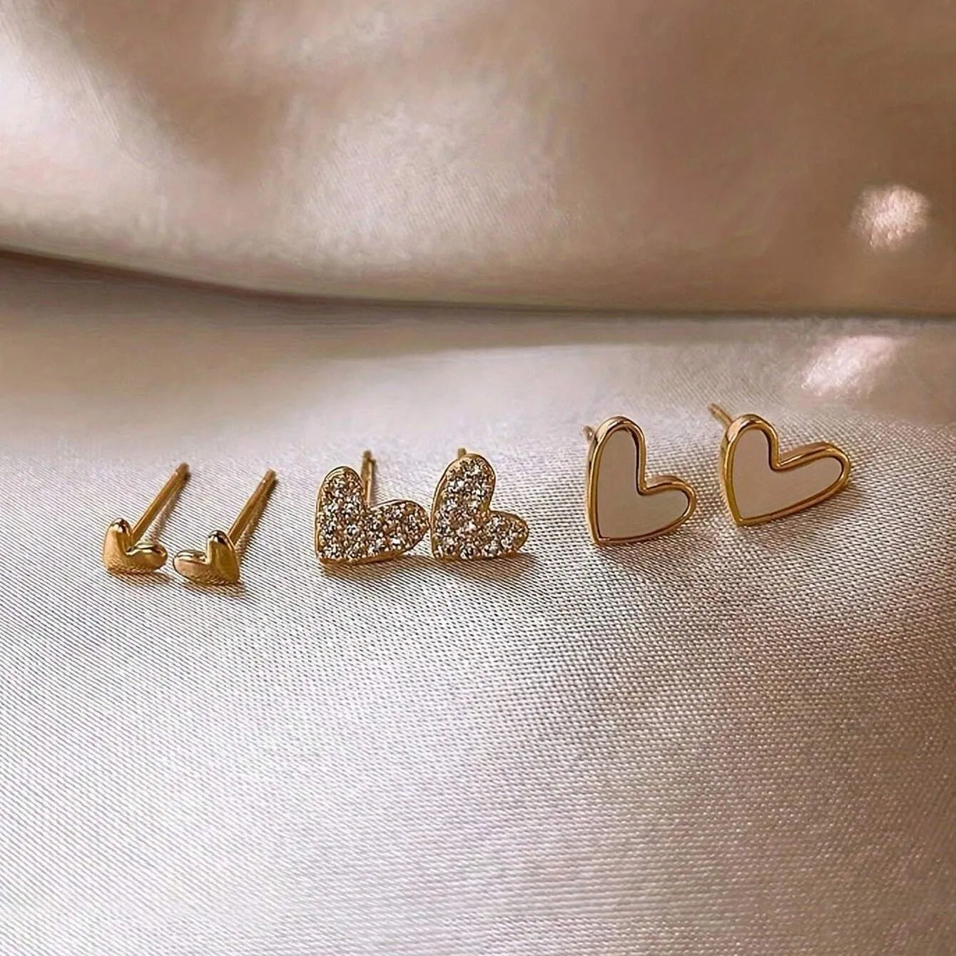 Three pairs of women's heart-shaped alloy earrings in electroplated colours on display