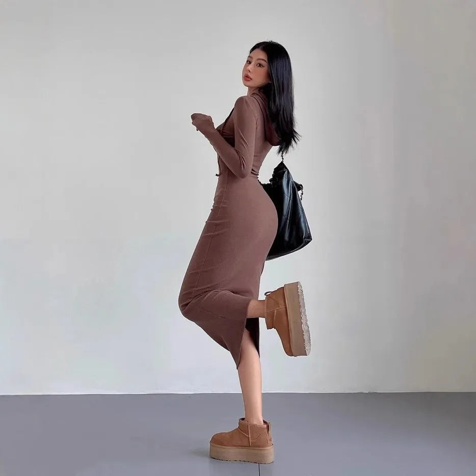 A woman wearing a light grey, long-sleeve polyester sheath dress with an over-the-knee length and high waist.