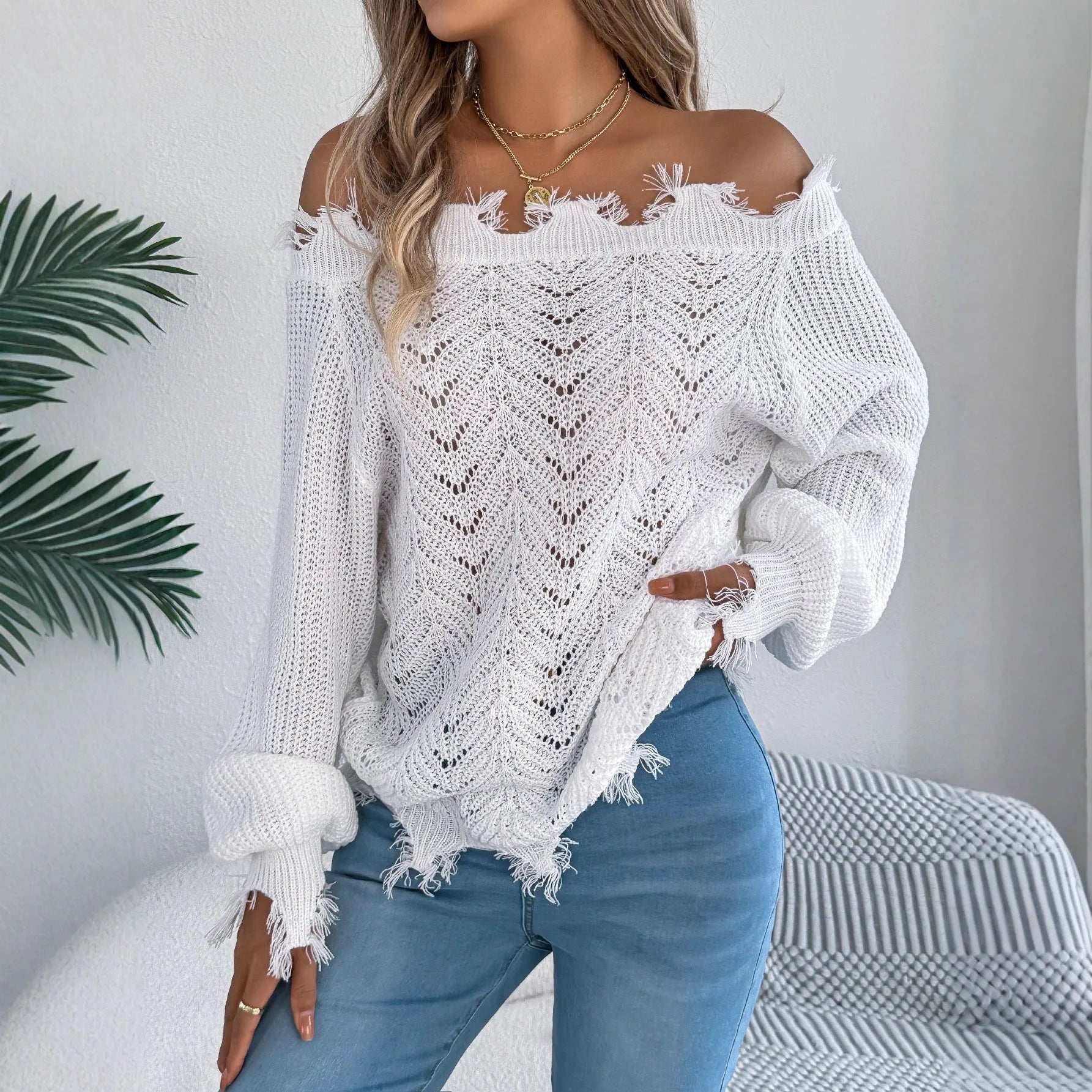 White hollow-out long-sleeved pullover sweater with an off-the-shoulder cut and regular sleeves on a hanger.