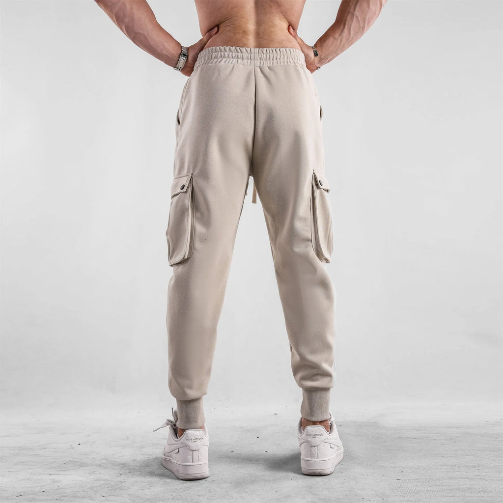 Man wearing loose light grey cotton trousers with ankle-tied cuffs and multiple pockets.