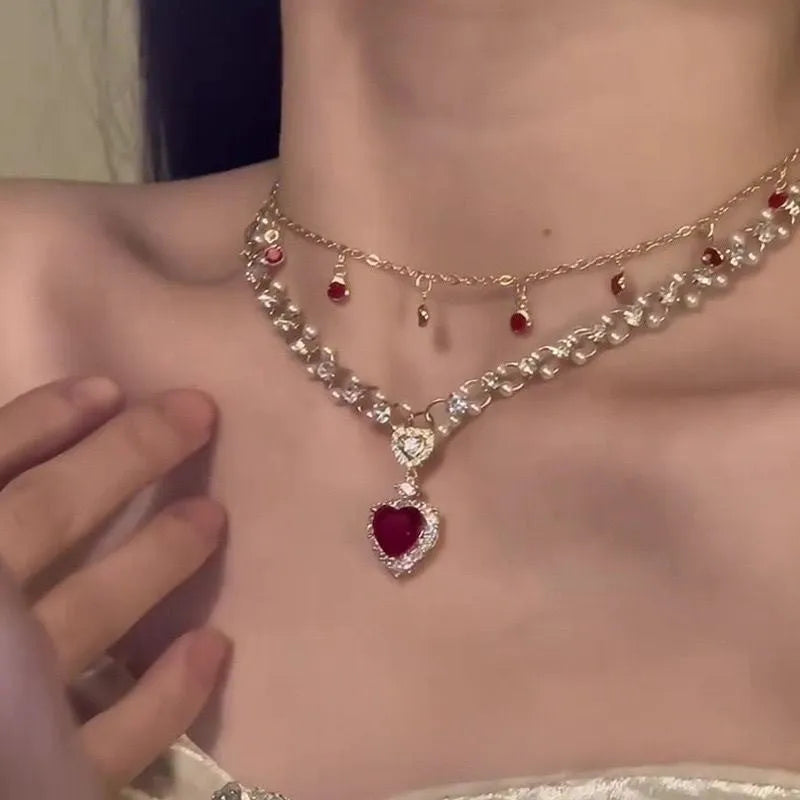 Gold tone double chain necklace with a central red love pearl pendant on an adjustable chain.