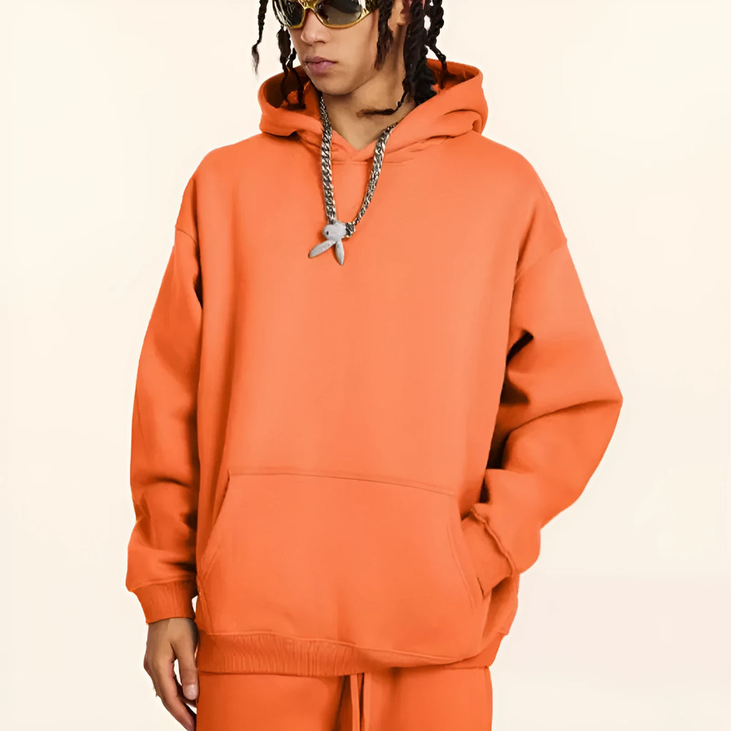 A man wearing a loose-fit, grey cotton hooded pullover sweater with drop-shoulder sleeves.