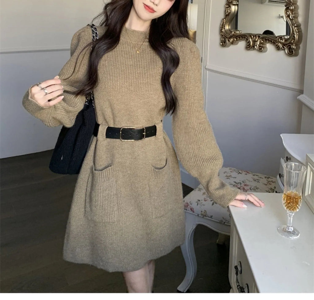 A woman wearing a long sleeve, loose knitted dress in a high-waist style with a black belt.