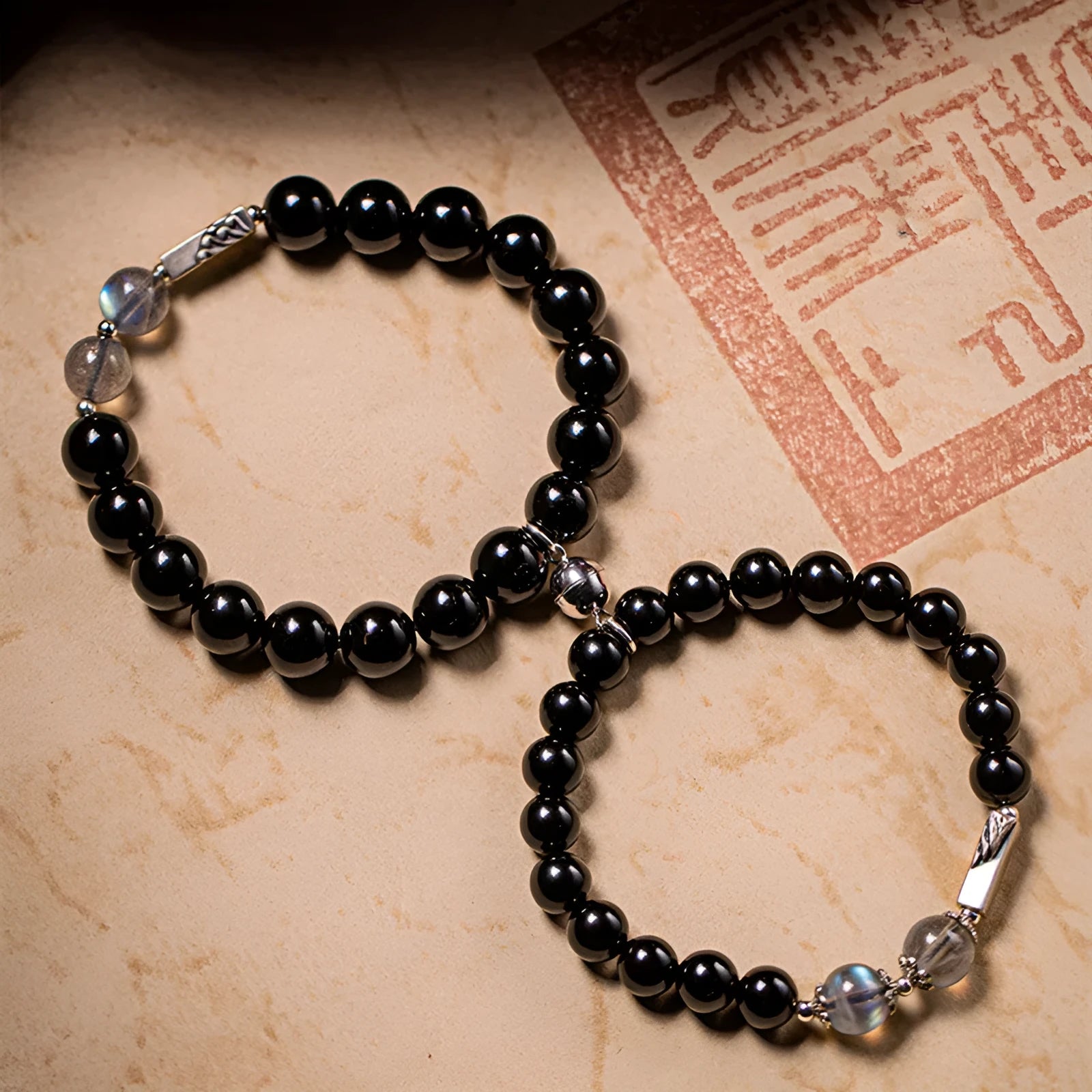 Black obsidian Buddha bead couple bracelets showing 8mm and 10mm sizes on a background.