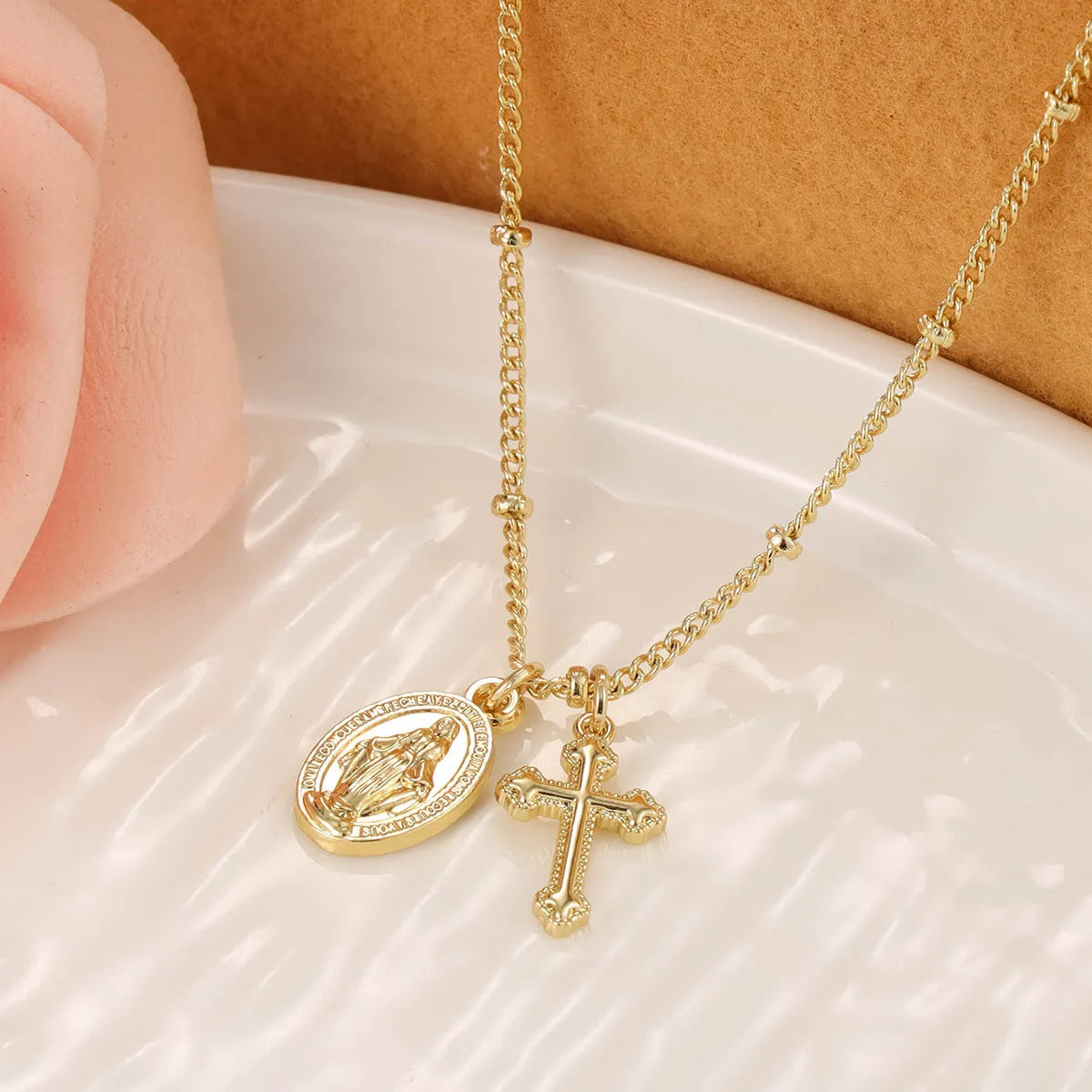 Gold geometric cross necklace with a Virgin Mary ornament pendant on a chain.