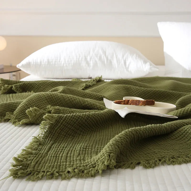 Four-layer cotton gauze blanket with tassel trim shown in avocado green colour.