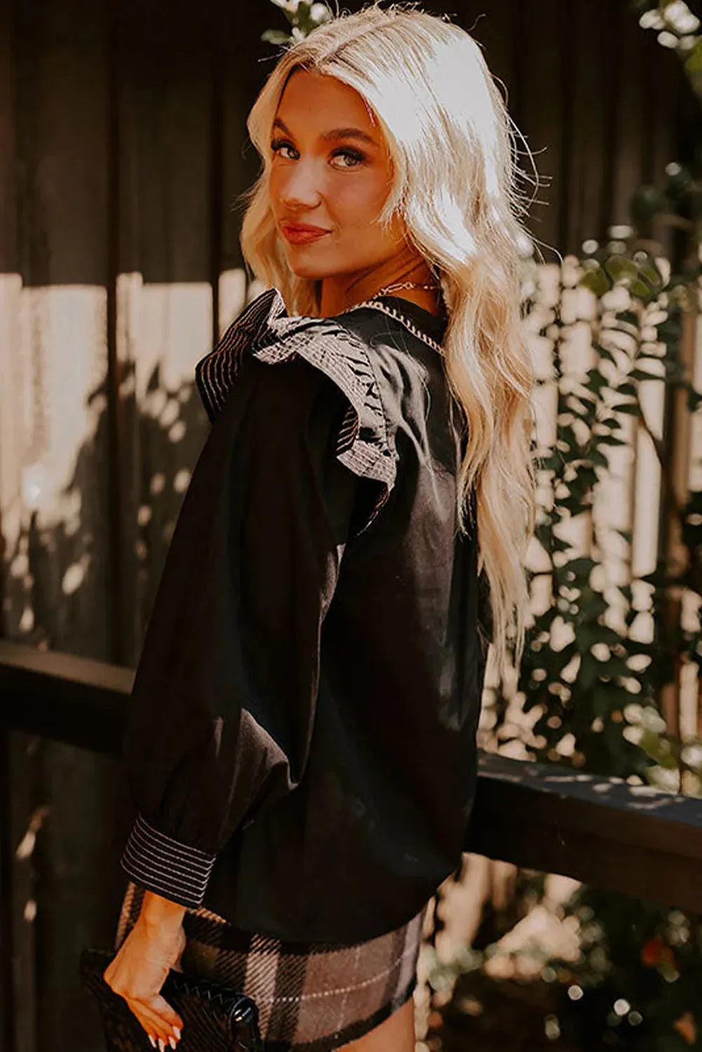 Black women's long sleeve blouse with V-neck, ruffle sleeves, and contrast stitching.