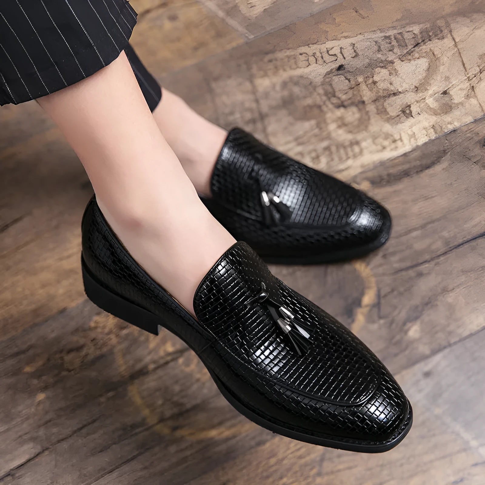 Men's black pointed slip-on business shoes with a tassel detail on the artificial PU leather upper.