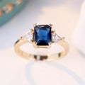 Women's rectangular copper ring in gold sapphire blue on a neutral background, showing its geometric band shape.