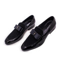 Men's black patent leather shoes with a gold tassel detail on a rubber sole.