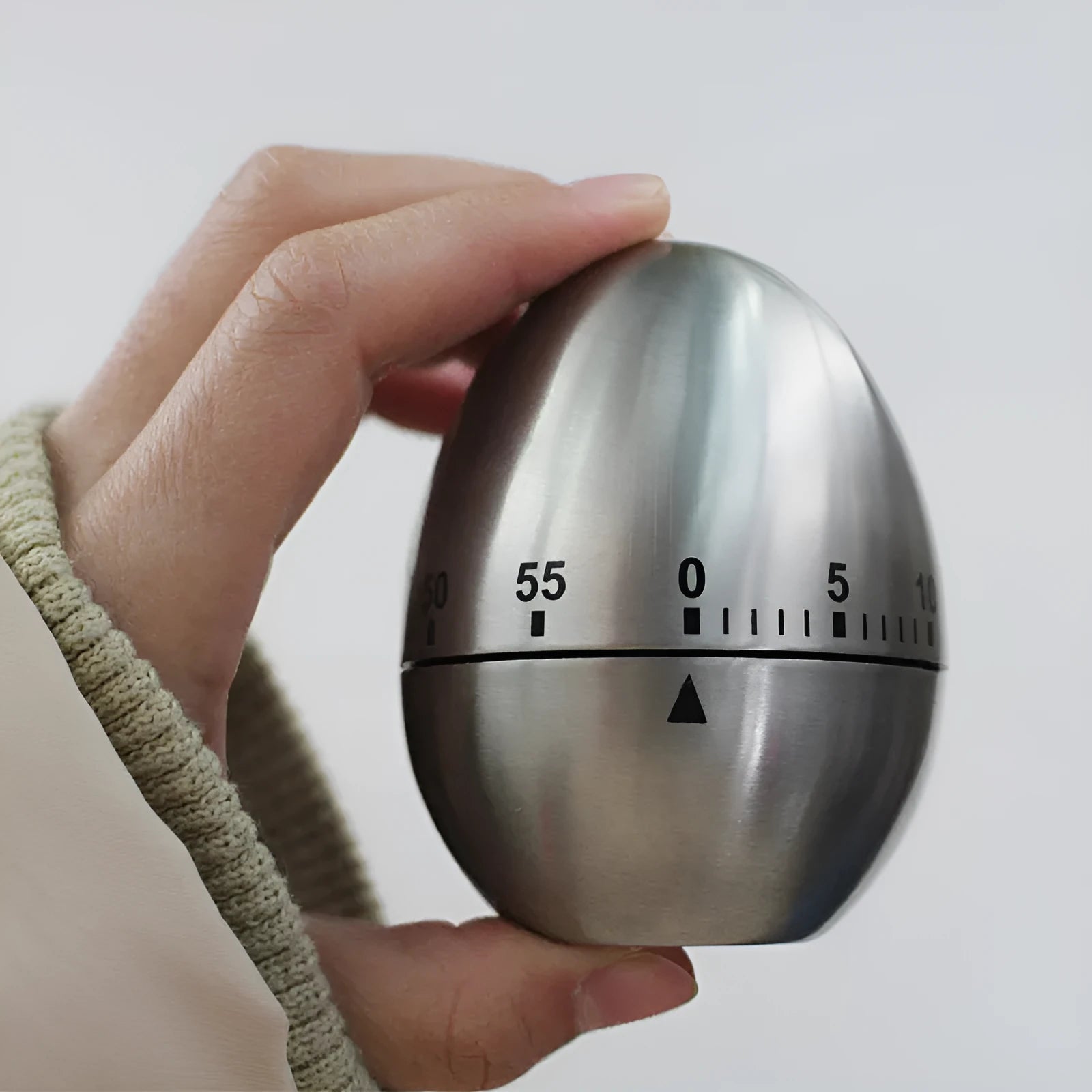 Stainless steel egg-shaped mechanical kitchen timer with manual dial.
