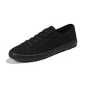 All black low-top canvas flat shoes with white laces and a rubber sole.