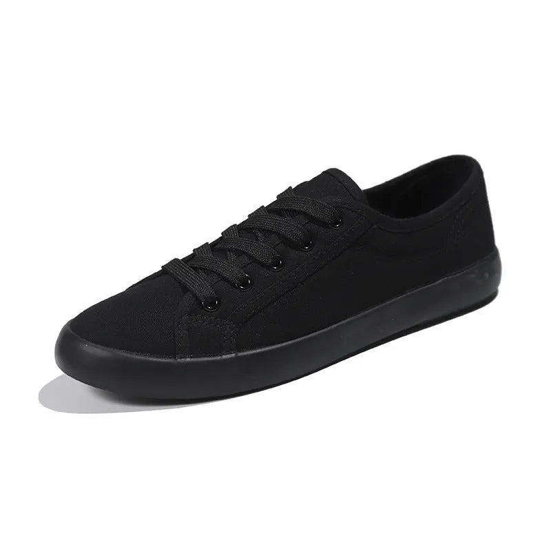 All black low-top canvas flat shoes with white laces and a rubber sole.