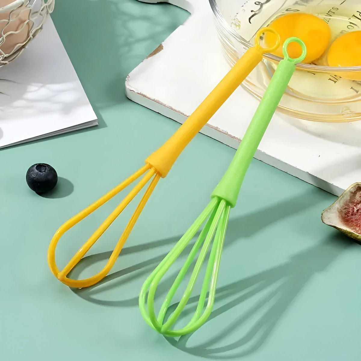 Plastic creative mini manual eggbeater in green and yellow, size 4x18.5 cm, on kitchen counter