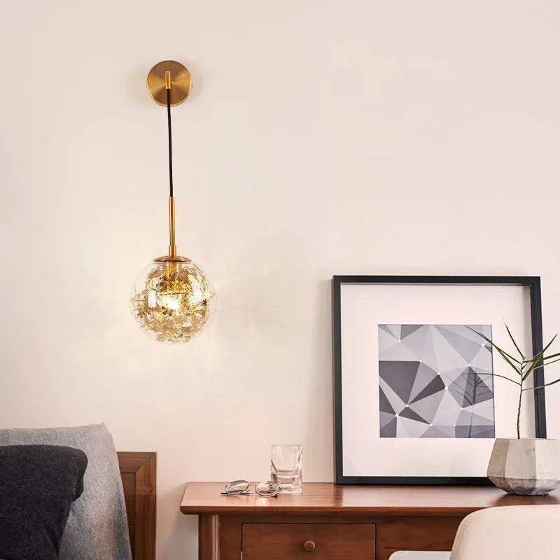 Glass wall lamp with decorative golden flower pattern on a white wall.