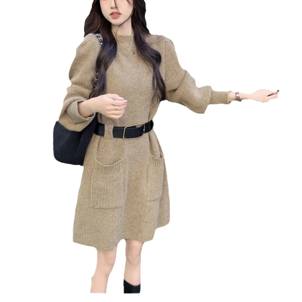 A woman wearing a long sleeve, loose knitted dress in a high-waist style with a black belt.
