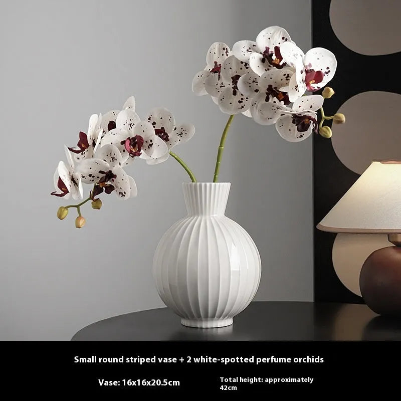 White ceramic ball vase with blue stripes and artificial blue orchid stems on a wooden table.