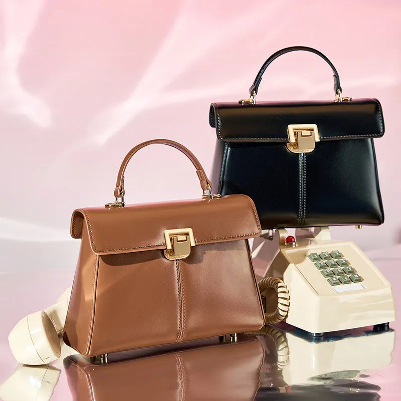 Black leather women's shoulder bag with vachette clasp, shown open to reveal internal zippered pocket.