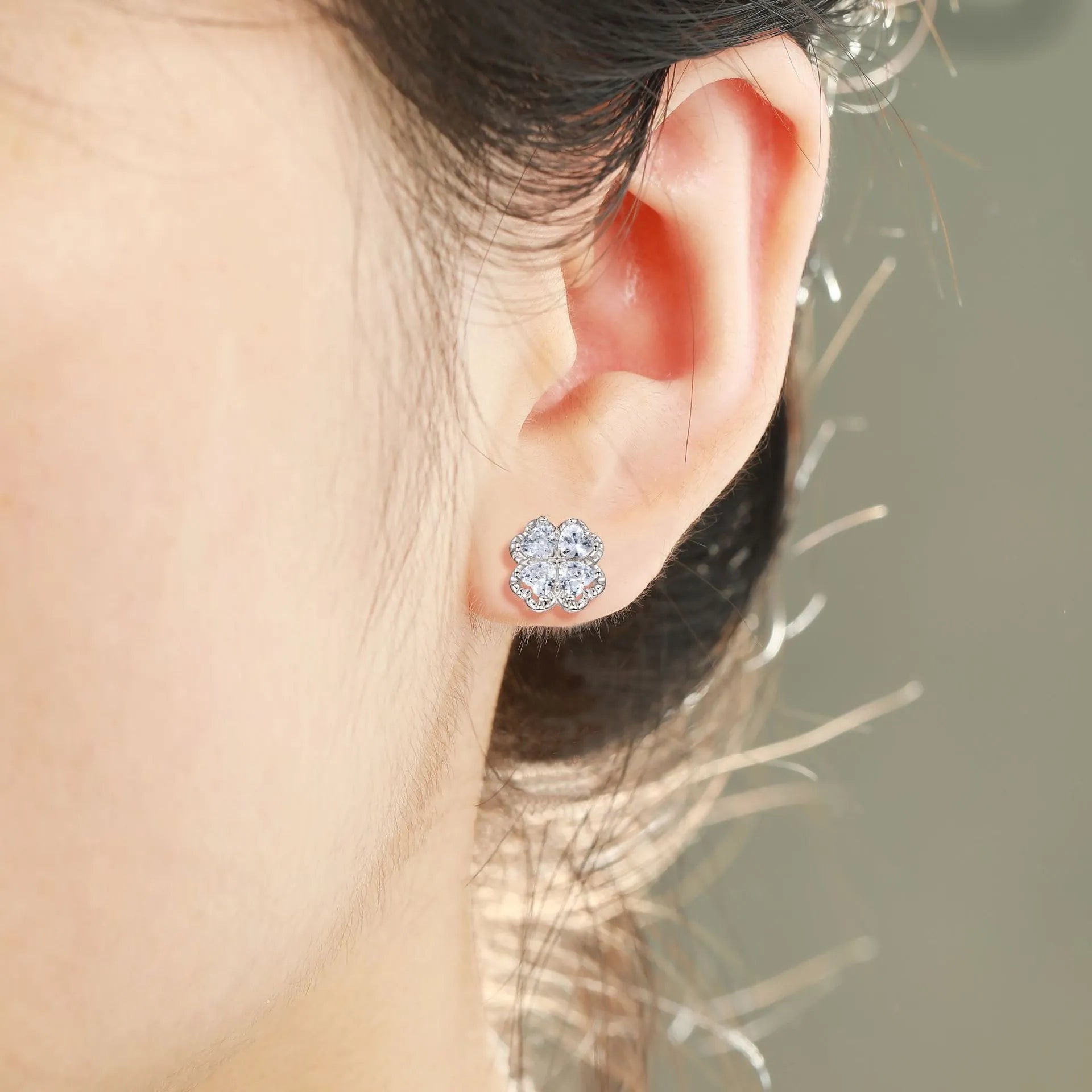 Close-up of a pair of heart-shaped 925 silver earrings with a four-leaf clover charm and zircon stones, in white gold colour.