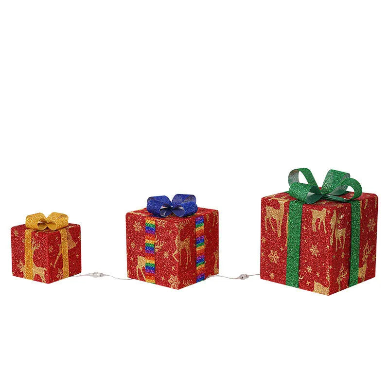 Set of three glittering pre-lit Christmas gift boxes with red bows, illuminated with warm white LED lights outdoors.