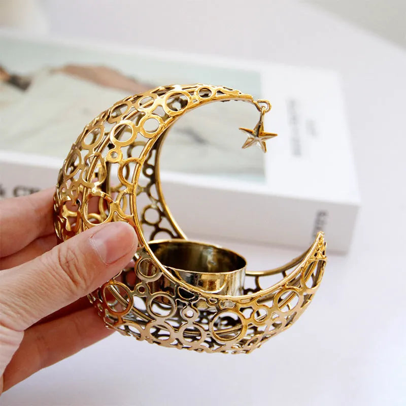 Gold metal crescent moon candle holder with hollow design on a dark surface