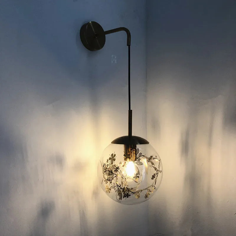 Glass wall lamp with decorative golden flower pattern on a white wall.