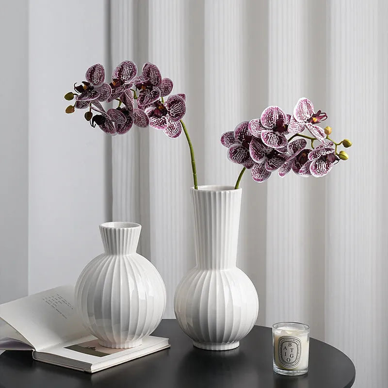White ceramic ball vase with blue stripes and artificial blue orchid stems on a wooden table.