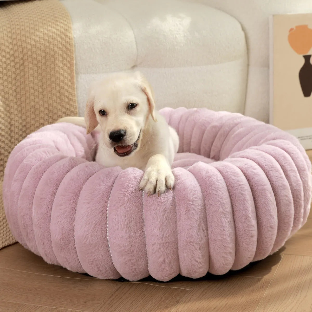 Round beige plush pet bed for a dog, shown in a medium size on a wooden floor.