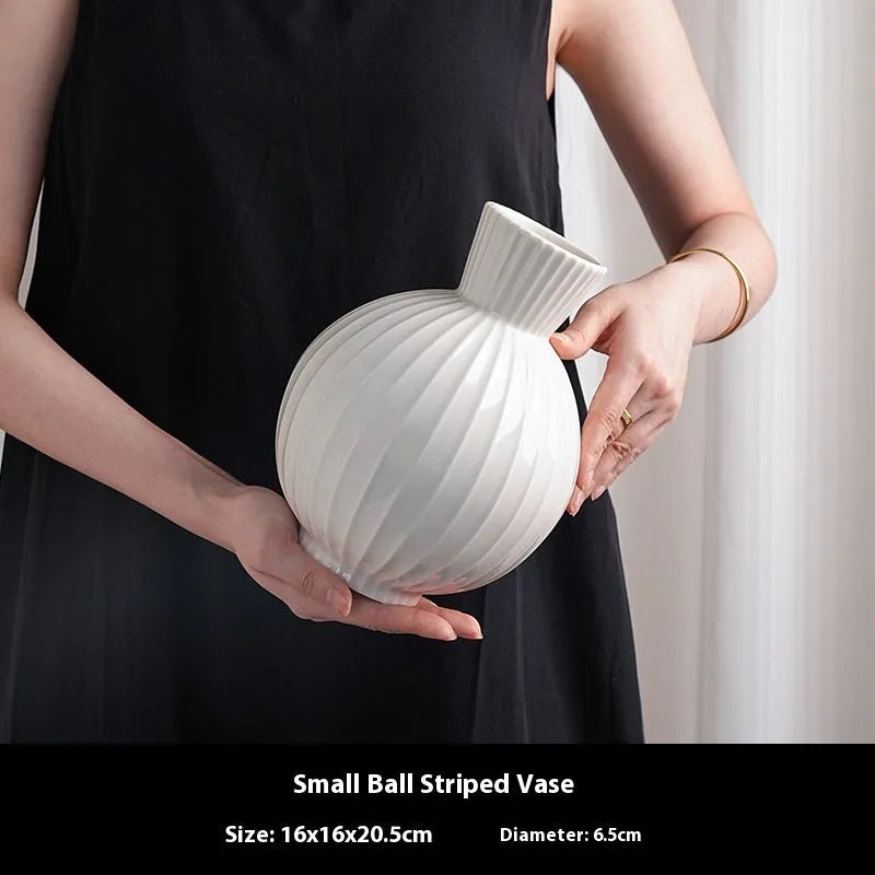 White ceramic ball vase with blue stripes and artificial blue orchid stems on a wooden table.