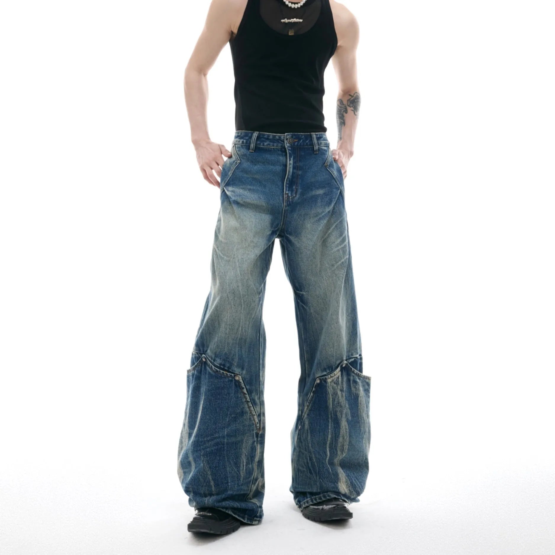 Man wearing loose fit verdant blue retro jeans with a curved knife cut and washed burst pattern.