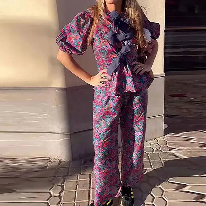 Women's floral print trouser suit set with tie-neck top and puffed sleeves.