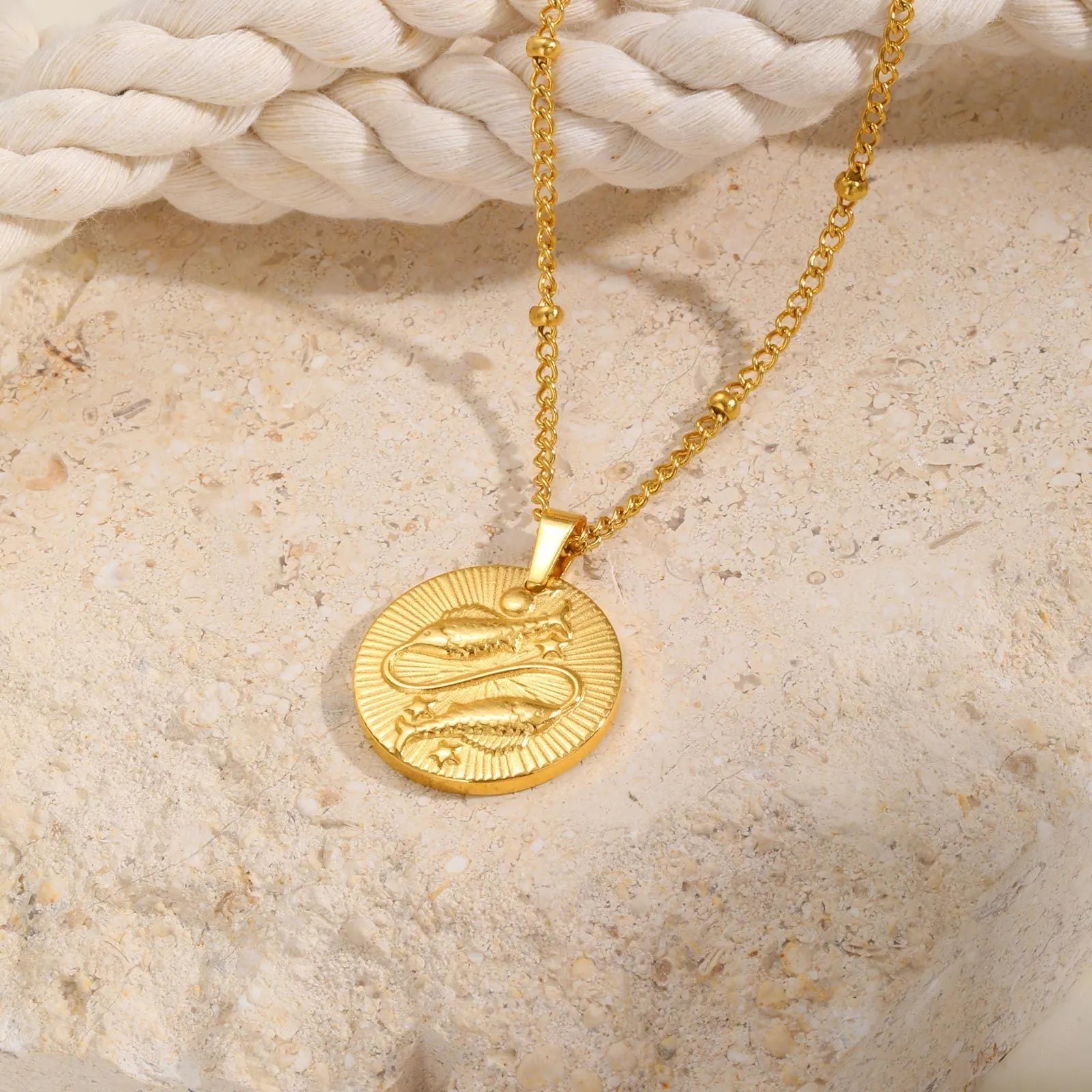 Stainless steel zodiac necklace with round pendant showing embossed constellation design on a cross chain.