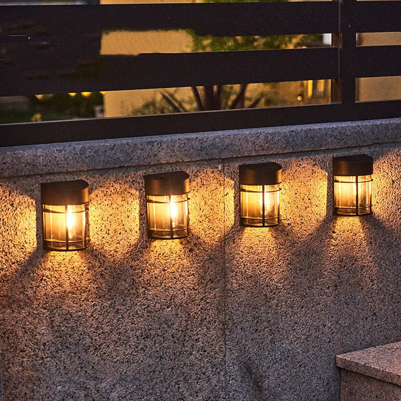 Small white solar-powered outdoor wall light with a dark solar panel on top, mounted on a wall.
