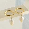 A pair of gold-coloured geometric stud earrings with a central white pearl on a white background.