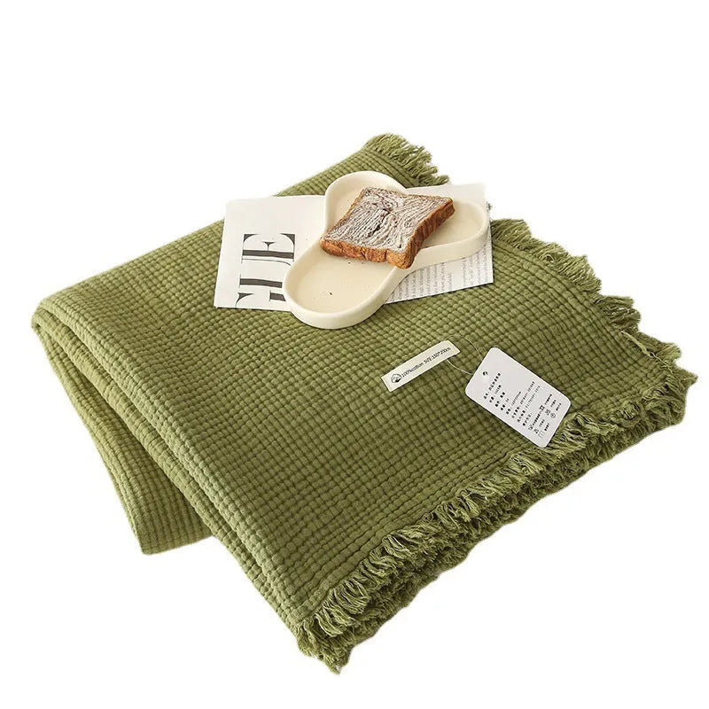 Four-layer cotton gauze blanket with tassel trim shown in avocado green colour.