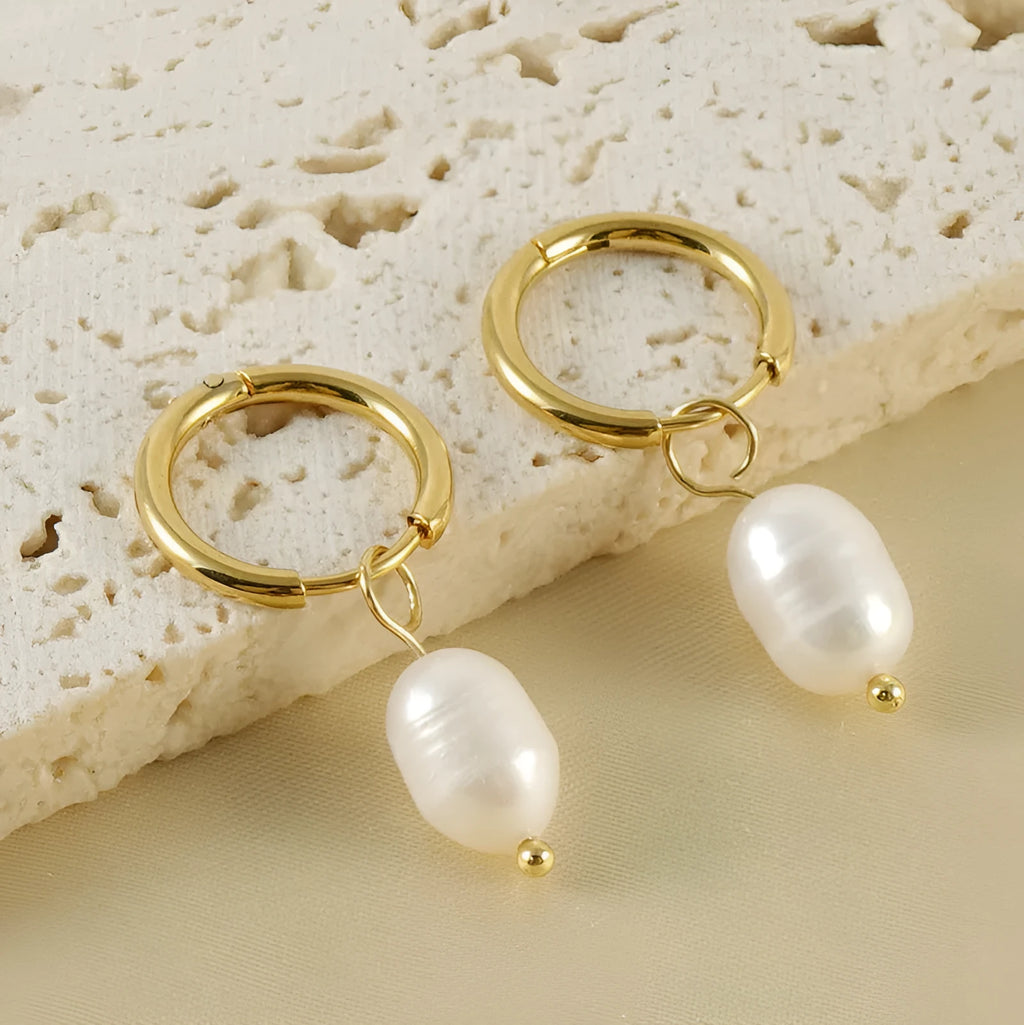 A pair of gold-coloured geometric stud earrings with a central white pearl on a white background.