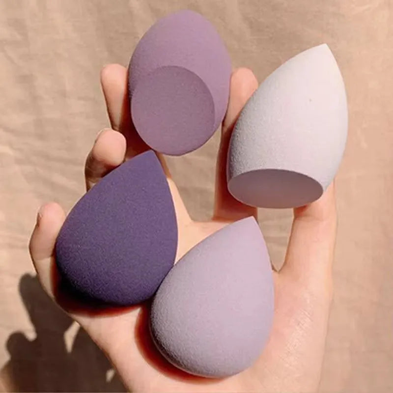 Set of seven differently shaped makeup sponges in various colours on pink background