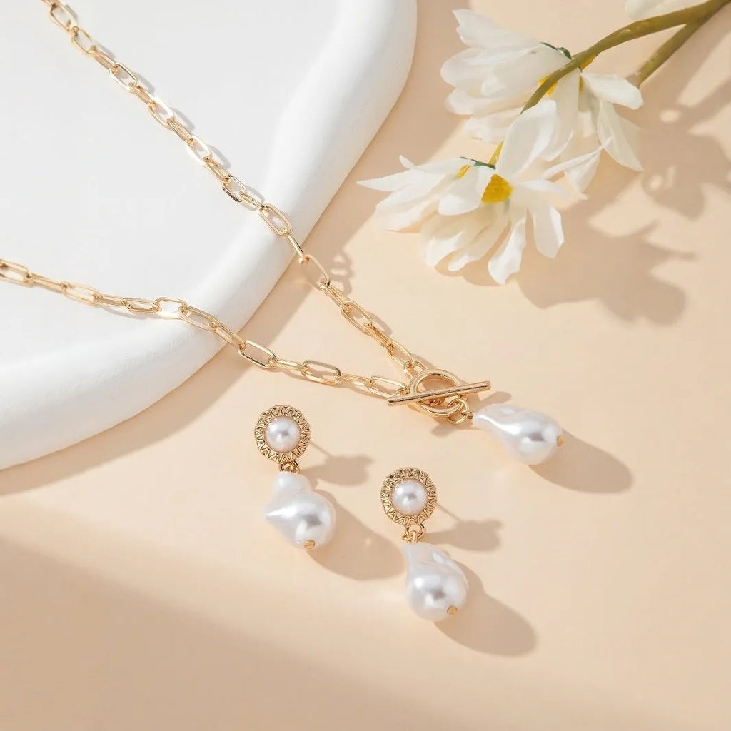 Gold-colour retro baroque pearl pendant necklace and matching ear studs set on a flat surface.