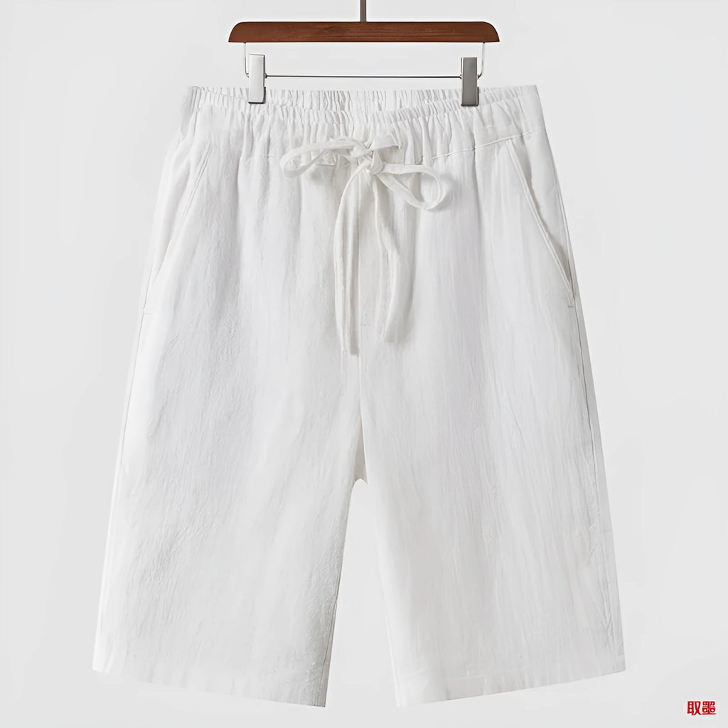 Men's beige linen shorts with loose cropped leg and elasticated waistband on a neutral background.
