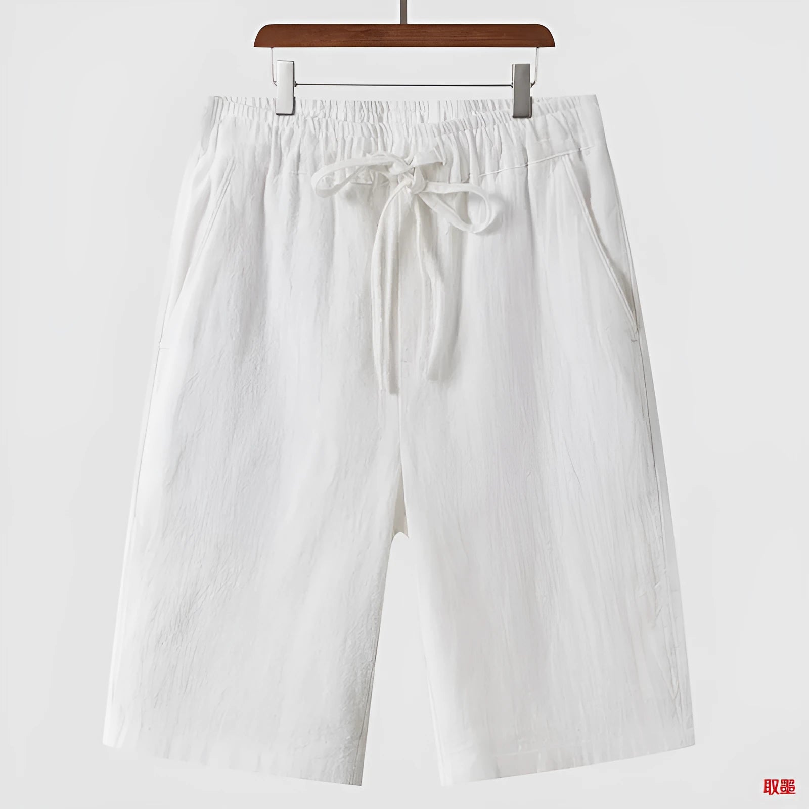 Men's beige linen shorts with loose cropped leg and elasticated waistband on a neutral background.