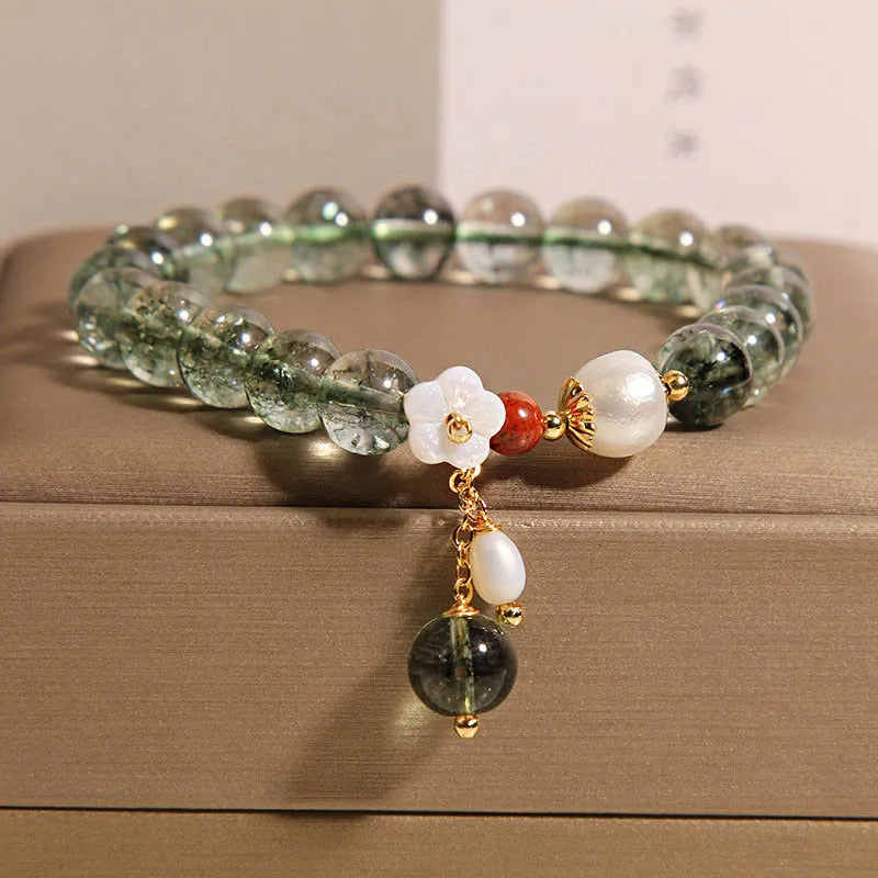 Green phantom quartz crystal bracelet with small shell flower design on woman's wrist.