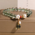 Green phantom quartz crystal bracelet with small shell flower design on woman's wrist.