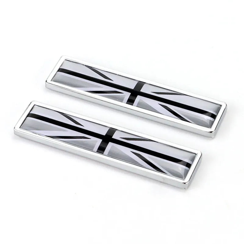 A pair of silver zinc alloy car badge labels with coloured national flag designs, shown at 58mm by 14mm scale.